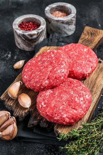 Obehandlade kalvhamburgerbiffar med örter och kryddor. Svart bakgrund. Ovanifrån — Stockfoto