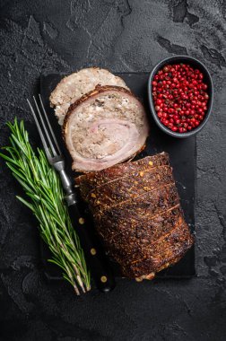 Pişmiş domuz rölesi Porchetta, mermer bir tahtanın üzerinde sarılmış domuz eti ve otlar. Siyah arka plan. Üst görünüm