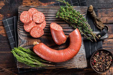 Kesme tahtasının üzerinde otlarla dilimlenmiş sucuk eti sosisi. Ahşap arka plan. Üst görünüm