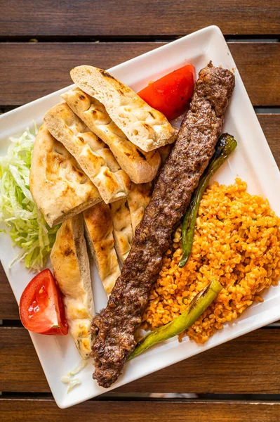 Kebab Adana turco en un plato con pimientos marinados, pan y arroz pilaf. Vista superior — Foto de Stock