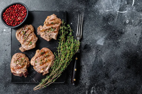 Côtelettes de longe d'agneau grillées steaks, escalopes sur une planche de marbre. Fond noir. Vue de dessus. Espace de copie — Photo