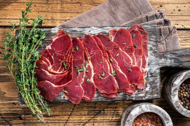 Kurutulmuş pastırma dilimleri, ahşap tahtada otlu sığır eti. Ahşap arka plan. Üst görünüm