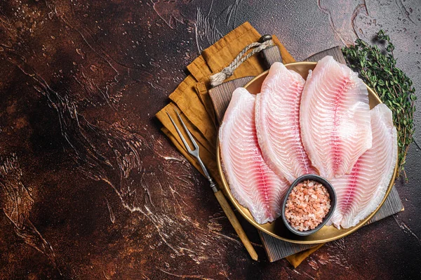 Rå fiskfilé av tilapia i en tallrik med kryddor. Mörk bakgrund. Högst upp. Kopiera utrymme — Stockfoto
