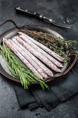 Spanish tapa mini fuet sausage with herbs. Black background. Top view.