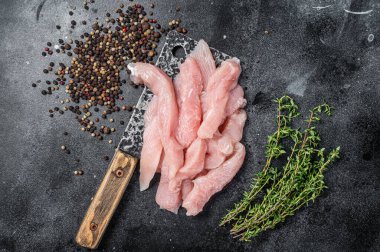 Slices of raw poultry meat on a butcher board with meat cleaver, chicken breast. Black background. Top view.