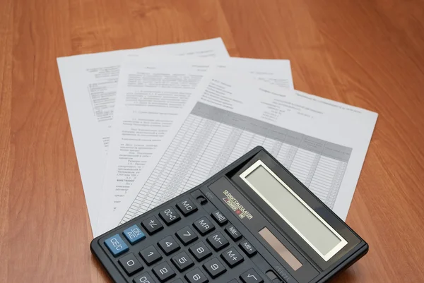 Calculadora con hojas de papel sobre fondo de madera — Foto de Stock