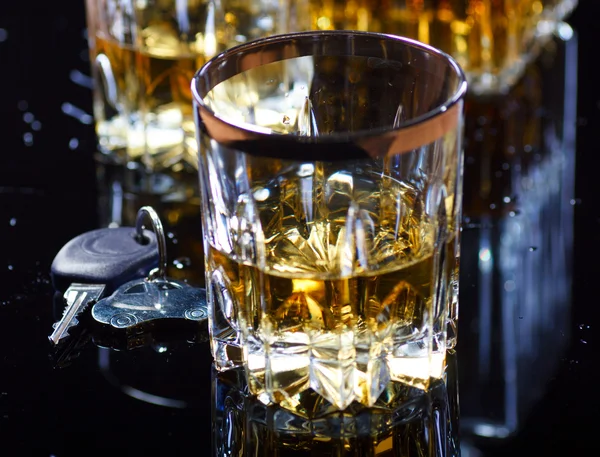 Autosleutels in de voorgrond en een glas whiskey — Stockfoto