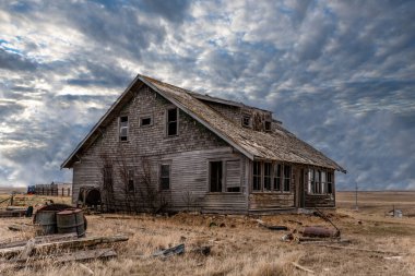 Saskatchewan ovalarında hurdalarla çevrili eski, terk edilmiş bir evin üzerinde mavi bir gökyüzü. 