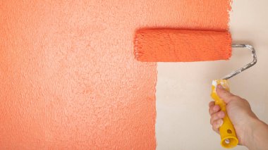peach wall painting, hand with roller the concept of renovation in the room copy space.