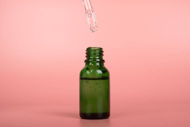 green cosmetic bottle with pipette on pink background,beauty skin care object.