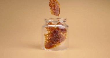 Kahverengi kenevir ağdalı cam kavanoz, turuncu arka planda sertleştirilmiş marihuana özü parçaları. Yüksek kalite 4k görüntü