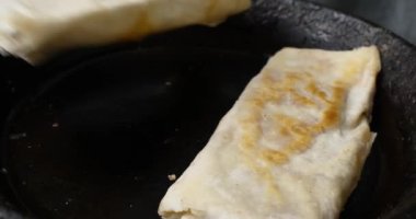 Tahta spatulalı bir el, domatesli peynirli rulo ve tavada pide sosisli sandviç çeviriyor. Yüksek kalite 4k görüntü