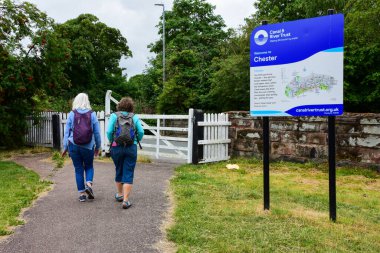 Chester, UK: Jul 3, 2022: A pair of female walkers pass an information sign at an access point between Chester City Centre and the Shropshire Union Canal.