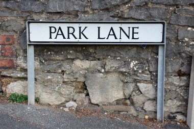 A street name sign for Park Lane mounted in front of a stone wall