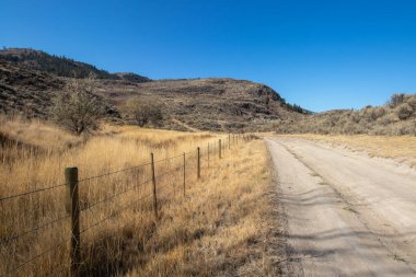 Kanada 'da güneşli bir günde Osoyoos, British Columbia' daki dağlarda tek şeritli toprak yol