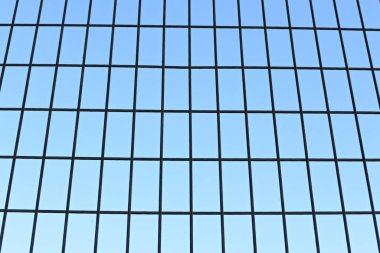Detalle de una reja o malla de hierro con el azul del cielo de fondo
