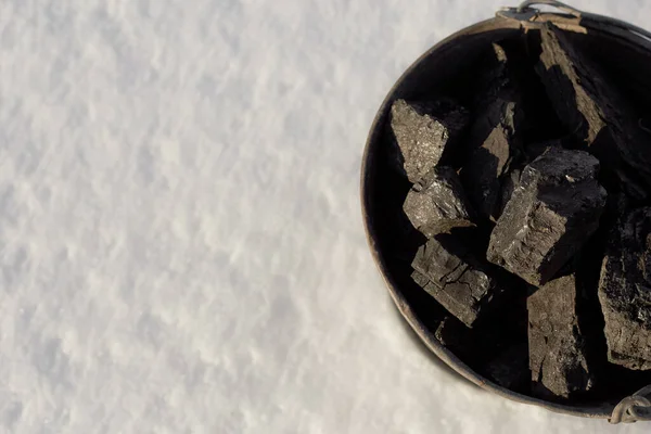 Černé uhlí v kbelíku na bílém pozadí sněhu, dává teplo v zimě — Stock fotografie