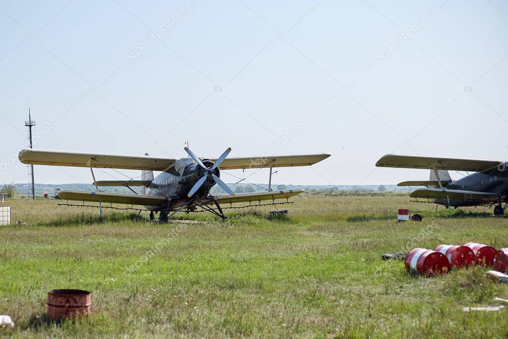 An old Soviet-era plane stands on a field airfield among barrels of fuel.