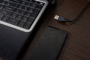 Siyah bir dizüstü bilgisayar ve akıllı telefon karanlık bir ahşap masa işi konseptinde yatıyor..