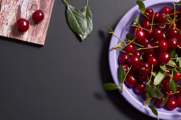 Fresh red cherry fruits on a plate on a wooden and black background. For postcard design.