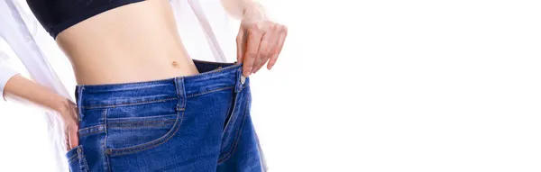 Cropped shot of young Caucasian slim woman wearing wide jeans and crop top demonstrating successful weight loss in front of white background. Diet and wellness concept — Stock Photo, Image