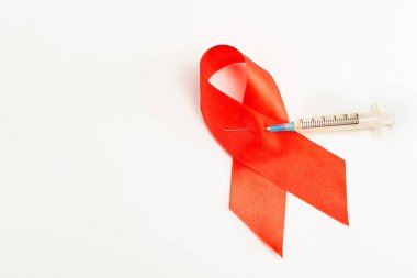 Sağlık ve tıp konsepti. AIDS farkındalığı. Kızıl AIDS farkındalık kurdelesi beyaz arka planda enjeksiyon şırıngası ile delindi. Uluslararası AIDS Günü