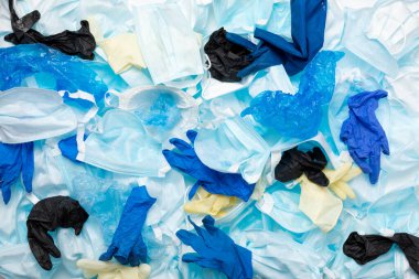 Kullanılmış koruyucu ekipman PPE eldivenleri, tek kullanımlık maskeler, arka planda çalışan tıbbi işçilerin ayakkabı kılıfları. COVID-19 salgınından sonra atık kirliliği