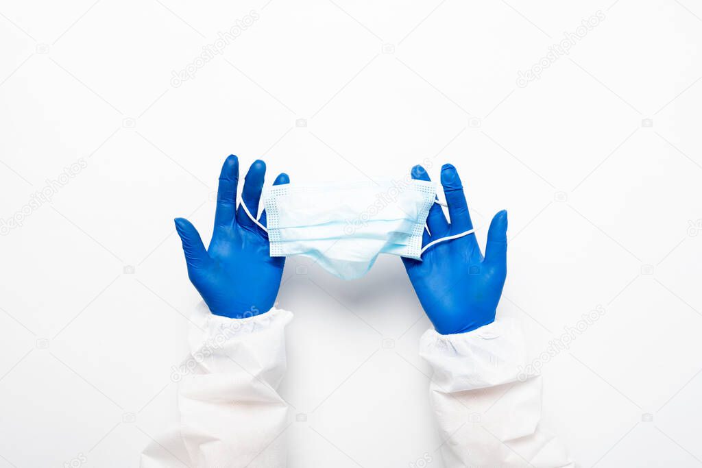Doctors hand in blue medical gloves holds anti-virus face mask on white background for pandemic, airborne diseases, outbreak, Covid19 concept