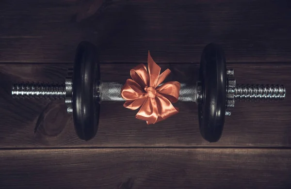 スポーツ用品の近くの木製のテーブルの贈り物のための赤い弓を持つ黒いダンベル 選手への贈り物だ健康的なライフスタイル スポーツ — ストック写真