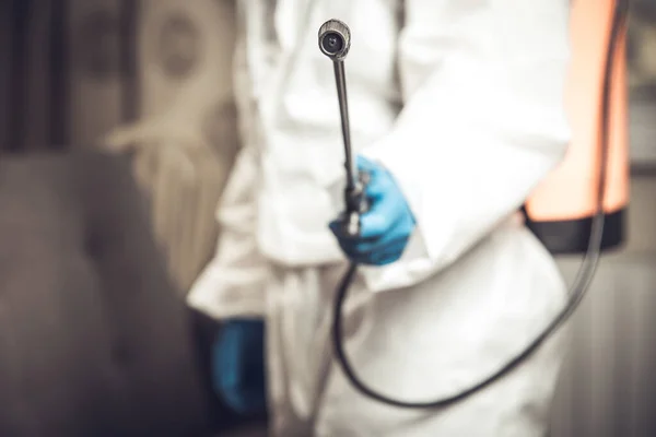 Spray gun with pesticides close-up. An exterminator in work clothes sprays pesticides from a spray bottle. Fight against insects in apartments and houses. Disinsection of premises.