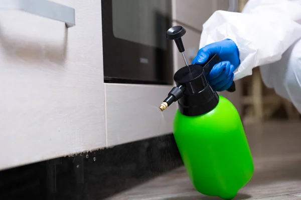 Spray gun with pesticides close-up. An exterminator in work clothes sprays pesticides from a spray bottle. Fight against insects in apartments and houses. Disinsection of premises.