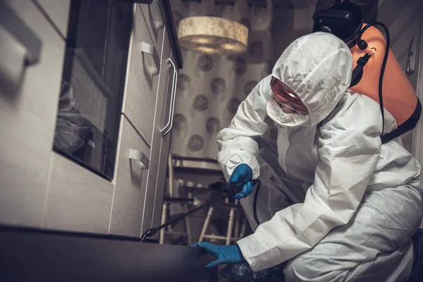 An exterminator in work clothes sprays pesticides with a spray gun. Fight against insects in apartments and houses. Disinsection of the premises.