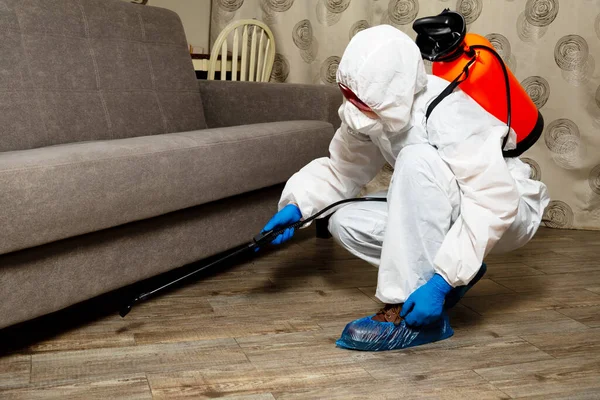 An exterminator in work clothes sprays pesticides with a spray gun. Fight against insects in apartments and houses. Disinsection of the premises.