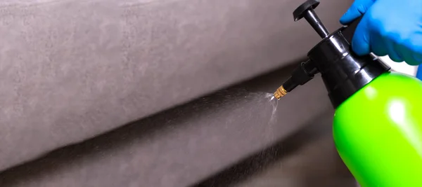 Spray gun with pesticides close-up. An exterminator in work clothes sprays pesticides from a spray bottle. Fight against insects in apartments and houses. Disinsection of premises.