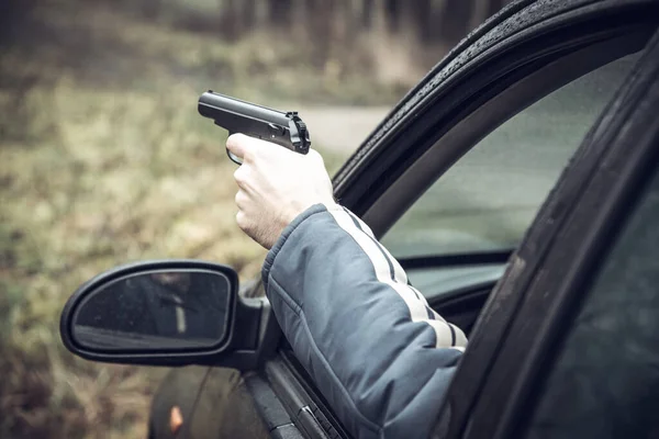Araba kullanan silahlı bir adam, elinde silah olan bir adam arabanın camından dışarı sarkmış. — Stok fotoğraf