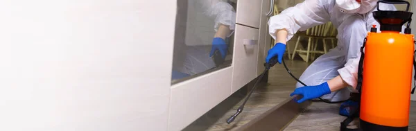 An exterminator in work clothes sprays pesticides with a spray gun. Fight against insects in apartments and houses. Disinsection of the premises — Stock Photo, Image