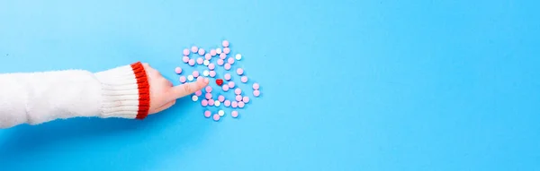 Roze pillen op een blauwe achtergrond met een hart in het midden. Hartgezondheidsconcept. Kinderen hand toont een hart onder roze pillen — Stockfoto