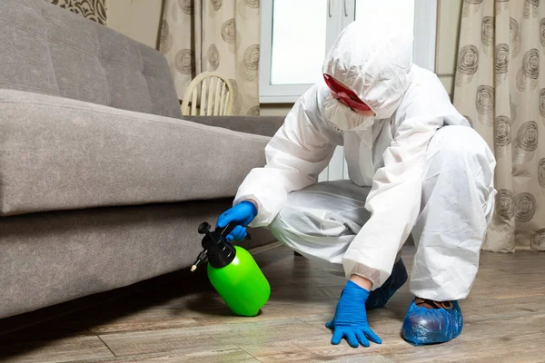 An exterminator in work clothes sprays pesticides with a spray gun. Fight against insects in apartments and houses. Disinsection of the premises Stock Photo