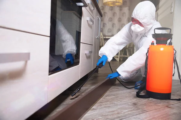 An exterminator in work clothes sprays pesticides with a spray gun. Fight against insects in apartments and houses. Disinsection of the premises Royalty Free Stock Images