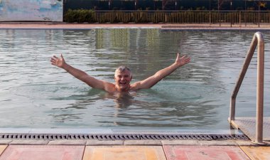 Bir adam açık havuzda termal suyla dinleniyor..