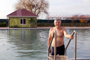 Havuzda termal suyu olan bir adam. Sonbaharda dinlenme merkezinde termal suyla yüzme havuzu.