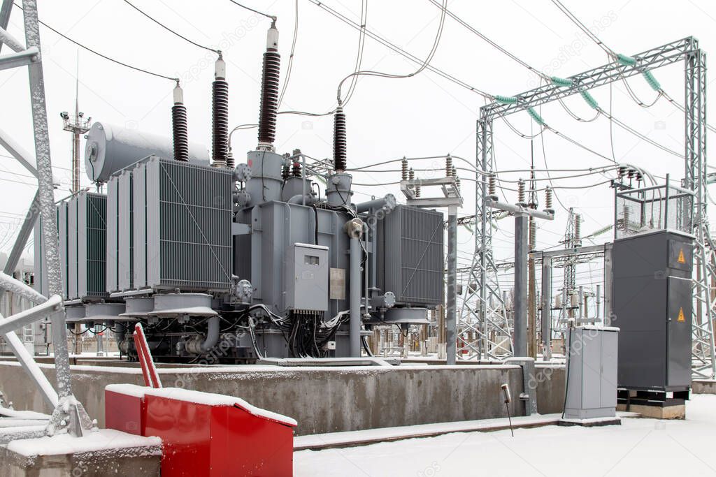 Power transformer at high voltage outdoor electrical substation in winter.