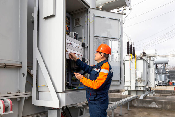 An electrician works at a power plant, near a transformer