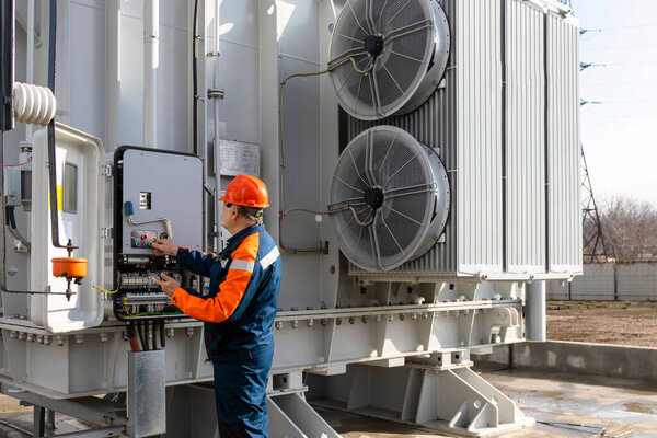 Electrical engineer inspecting electrical systems in equipment control cabinet using data from tablet