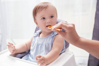Mavi elbiseli bebek annesi tarafından kaşıkla besleniyor.