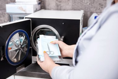 Otoklavda sterilizasyon için hazırlanmış aletleri tutan eller