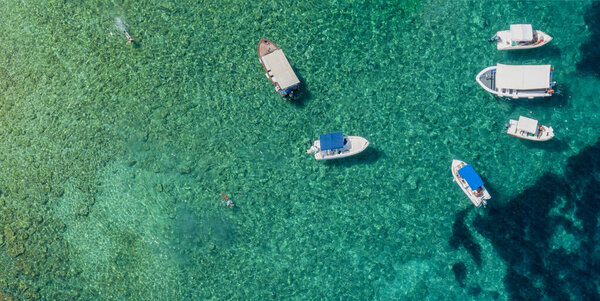 Aerial view of floating boats moored on a transparent sea. Relax on the Ionian Sea. Bathers. Corfu island, Limni beach Glyko. Greece