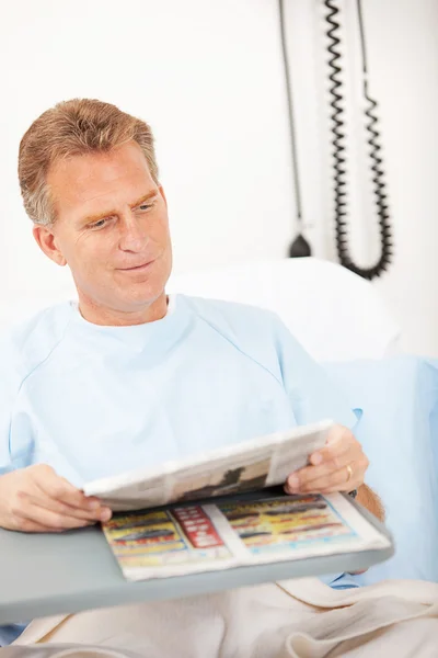 Hastane: Erkek hasta hastane yatağında kağıt okur. — Stok fotoğraf