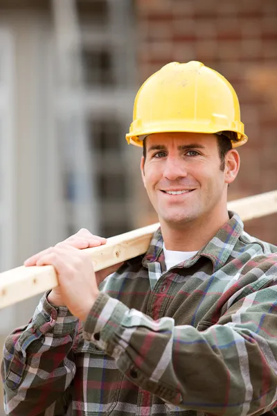 Construção: Suportes do trabalhador com 2x4 no ombro — Fotografia de Stock
