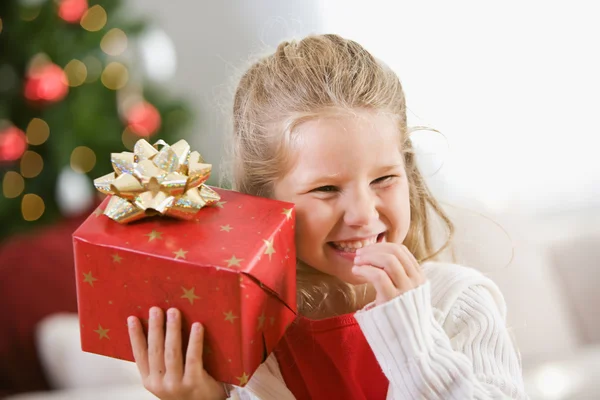 Natal: Menina jovem detém presente de Natal ao ouvido — Fotografia de Stock